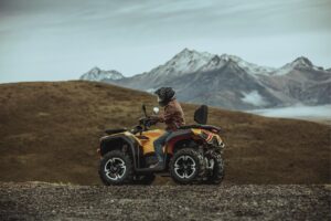 Person mit Helm fährt gelbes ATV Modell Guardian 500 auf Schotterweg vor Berglandschaft