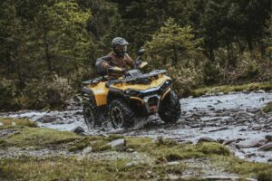 Person mSchutzkleidung fährt gelbes ATV Modell Guardian 500 durch einen flachen Bach