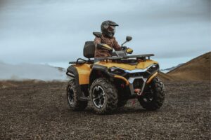 Person mit Helm und Schutzkleidung fährt gelbes ATV Guardian 500 auf unebenem Gelände
